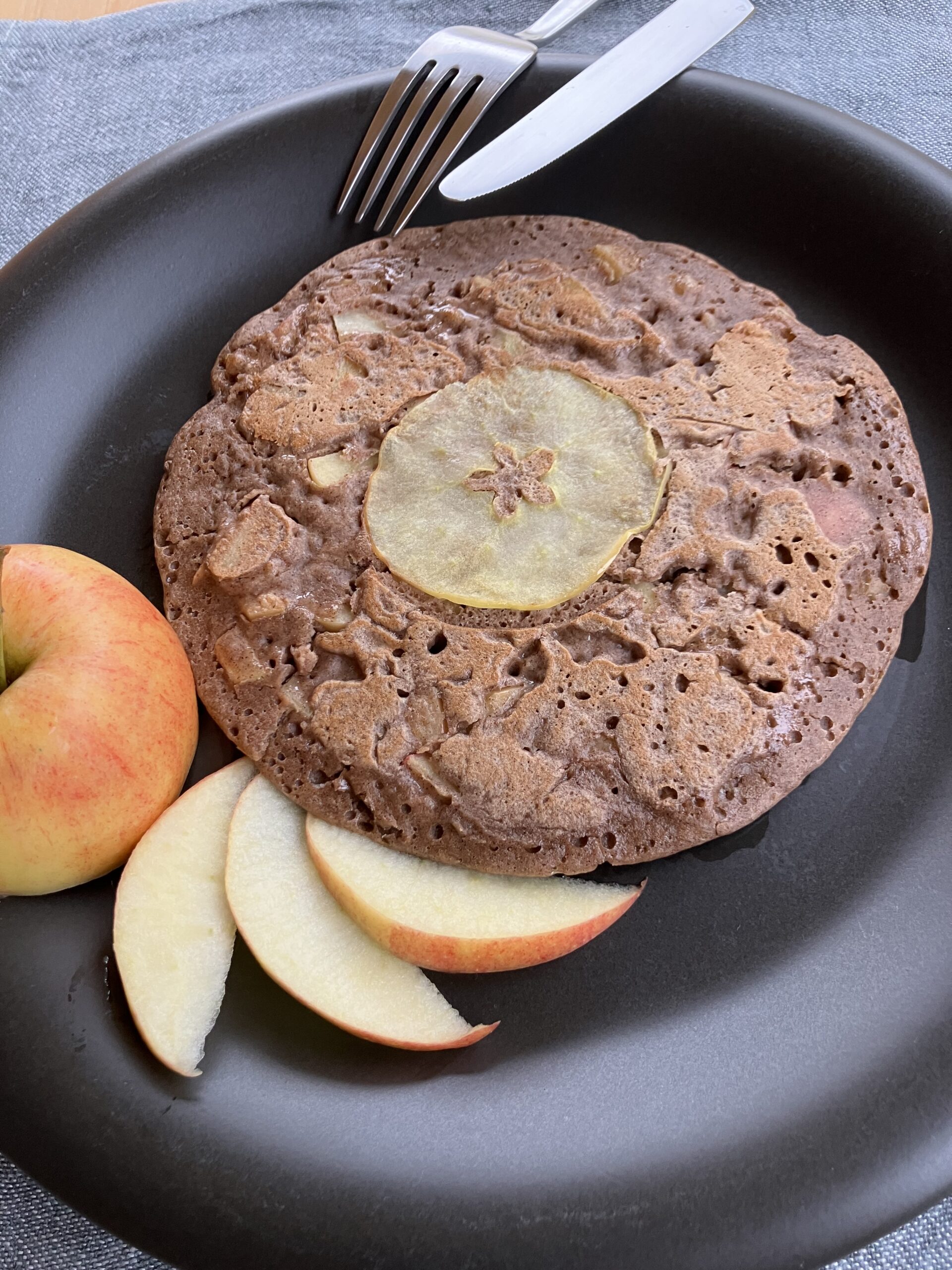 Une galette à la farine de sarrasin et de châtaignes, agrémentées de pommes, sur une assiette noire.