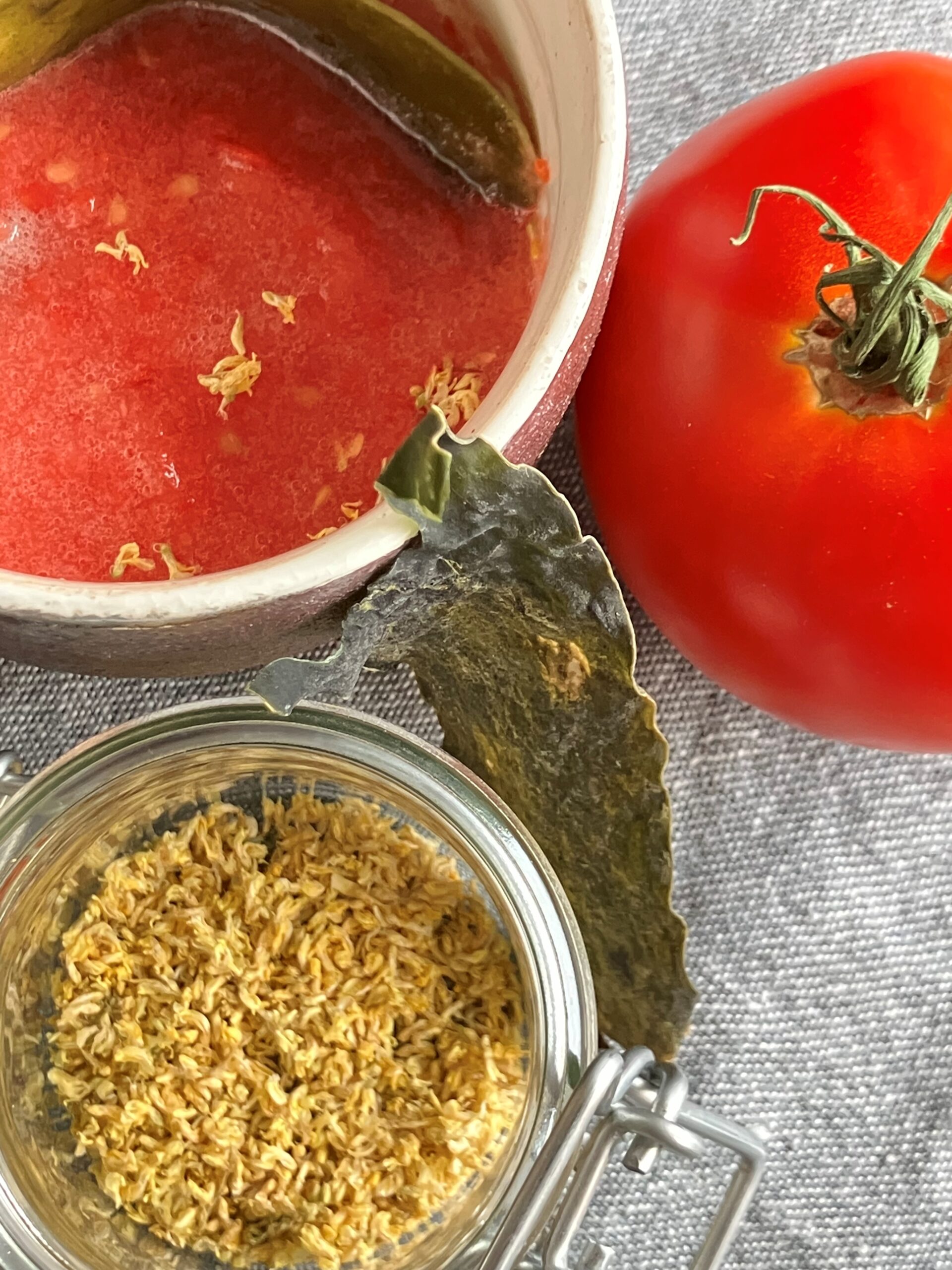 Un bol avec une dashi de tomate cru, une tomate, des fleurs de mélilot et du kombu